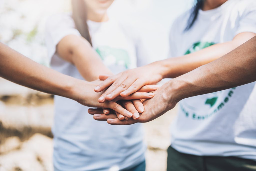 un groupe de personnes réunies, posant leurs mains les unes sur les autres en signe d'unité et de solidarité. l'ambiance renforce le message de collaboration et d'entraide et l'importance des actions communautaires.