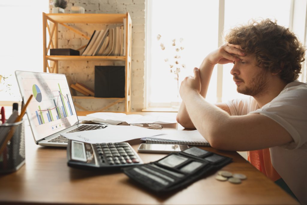 Homme regardant l'écran de son ordinateur l'air inquiet, sur sa table une calculatrice et son porte feuille.